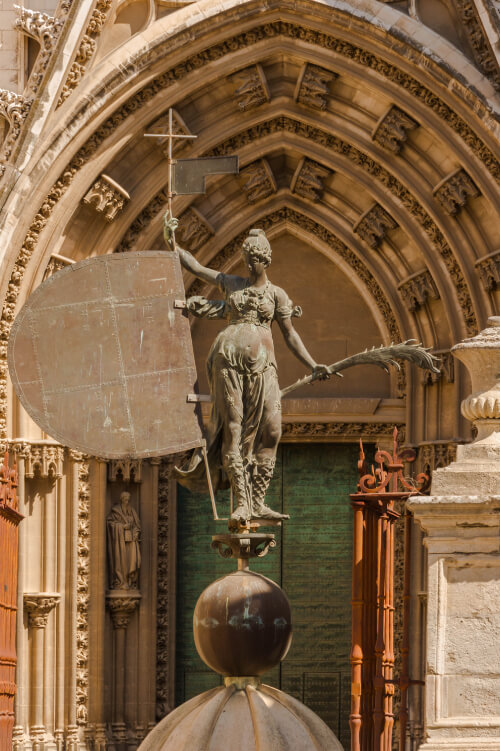 Réplica en bronce del Giraldillo, con la palma y el lábaro, ante una portada de la Catedral de Sevilla